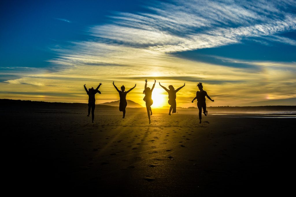 Five excited people jumping into the air, with the lighting from the sun behind them making them look like Silhouettes.